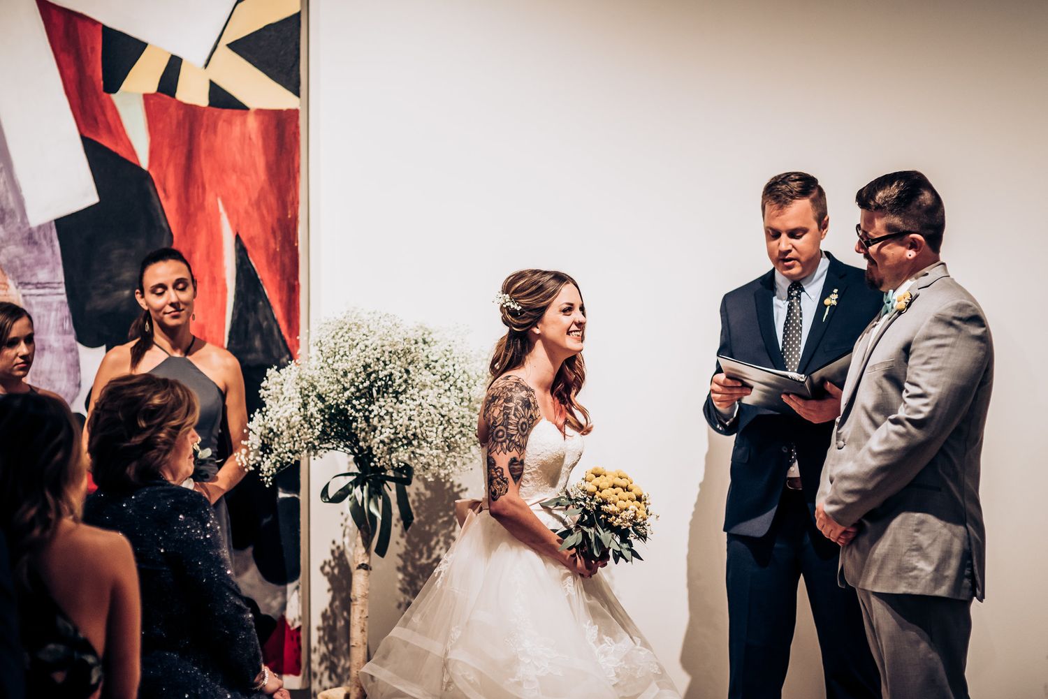 Wedding ceremony taking place in modern art gallery space with abstract paintings.