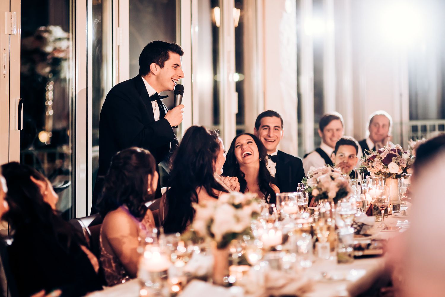 Wedding guests gathered around an elegantly set dinner table with glowing candlelight during an evening reception.