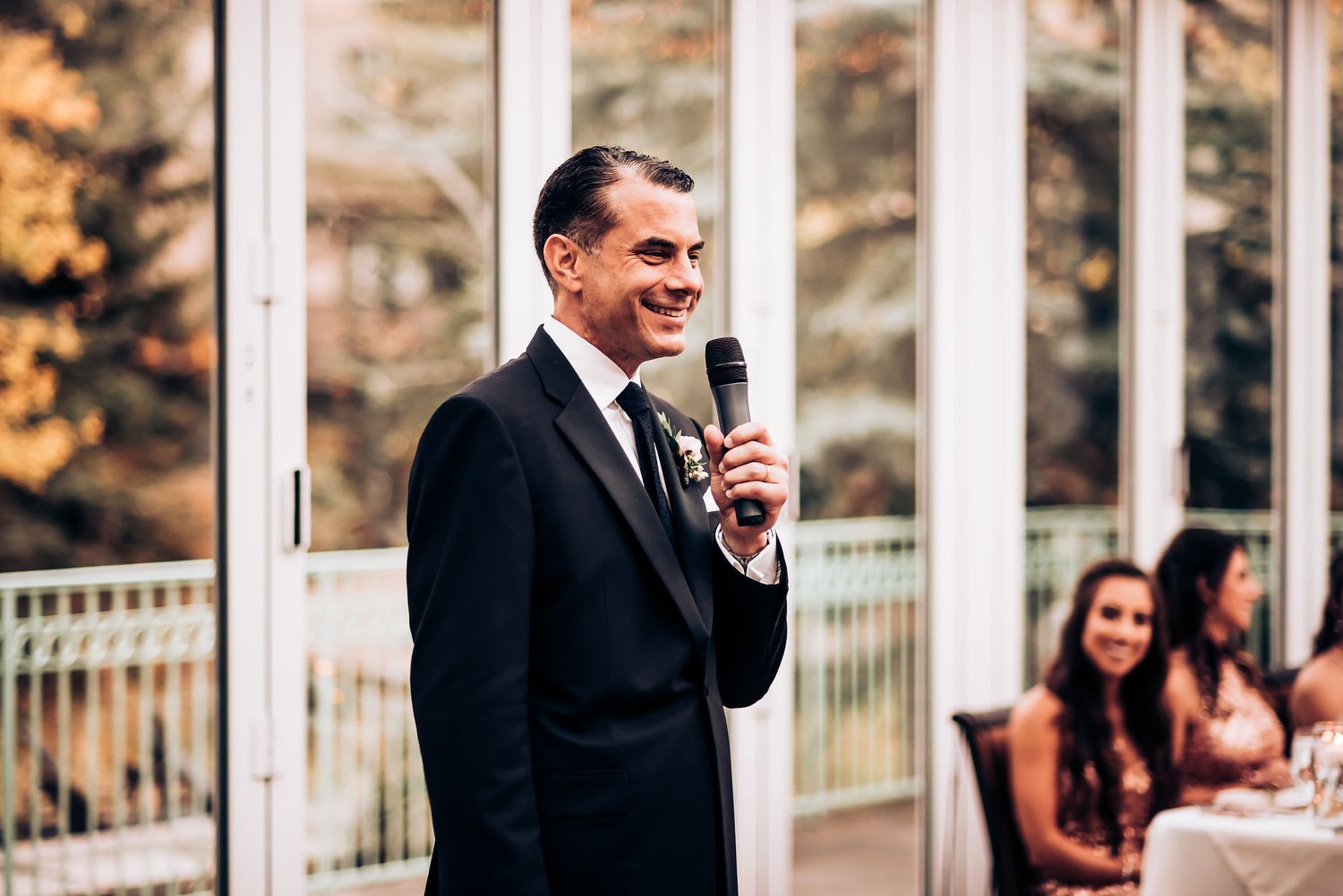 Speech being delivered at an elegant event with glass windows in background.