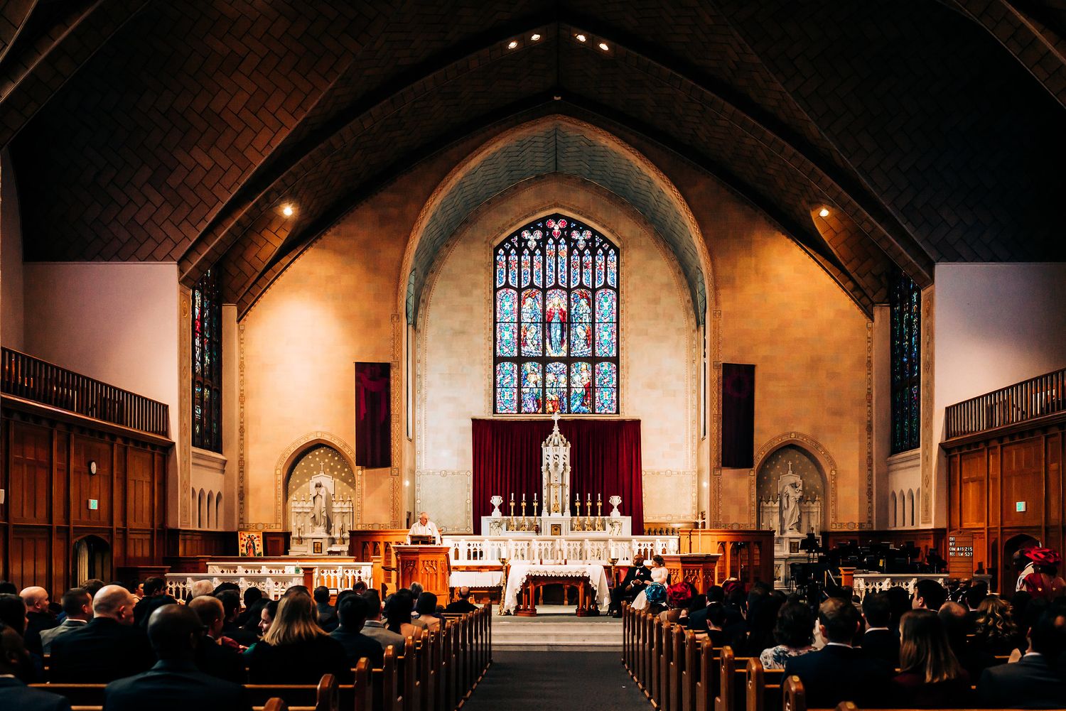 Interior of traditional church with vaulted ceiling and stained glass windows during wedding ceremony.