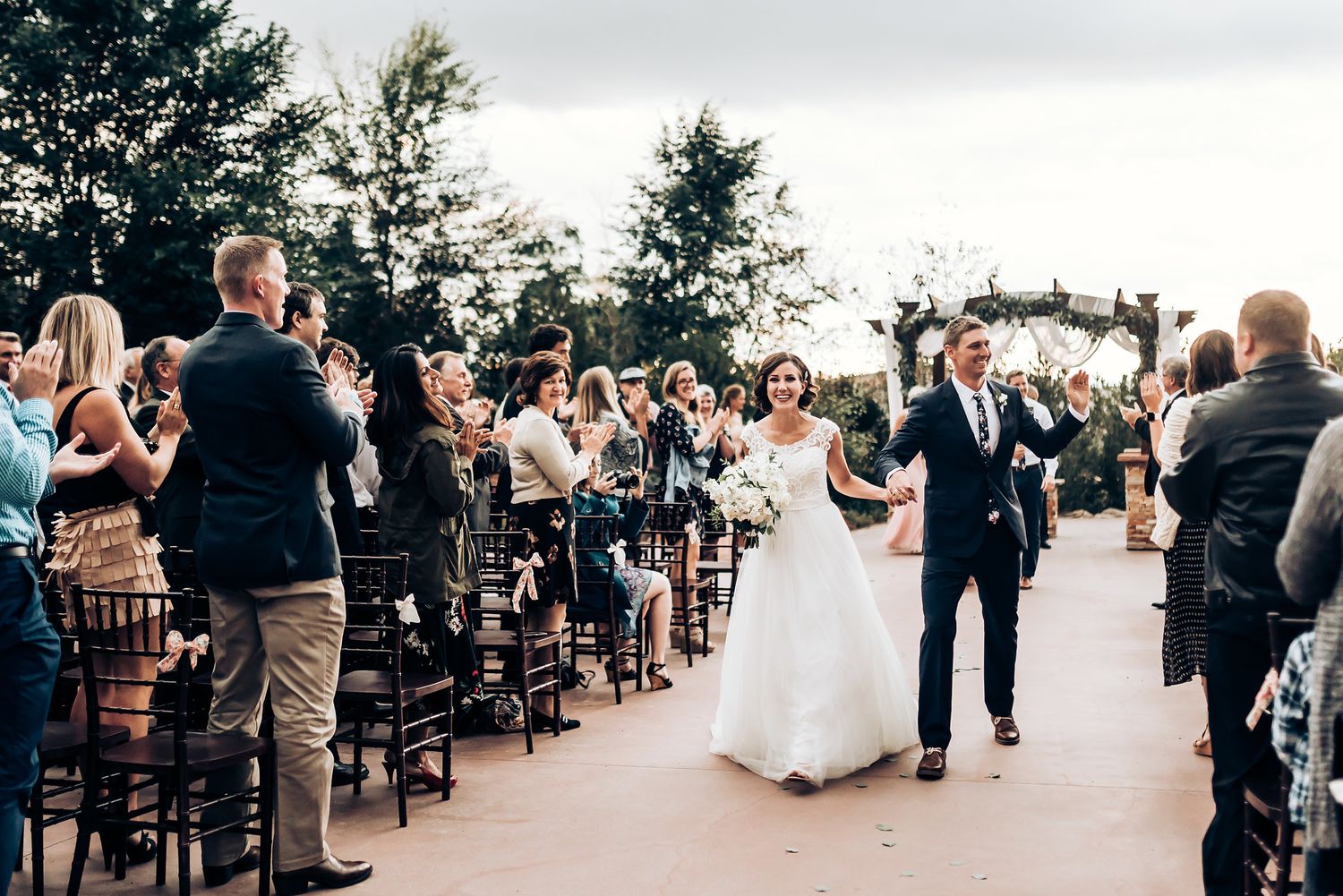 Couple making their grand exit while guests stand and celebrate at outdoor wedding venue.