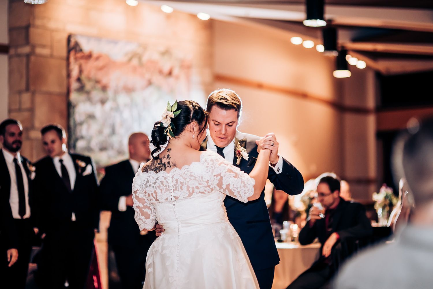 A romantic wedding dance moment captured under warm lighting and exposed ceiling beams.