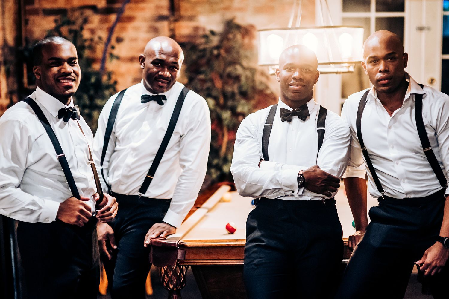 Groomsmen in white shirts and suspenders pose together at the venue.