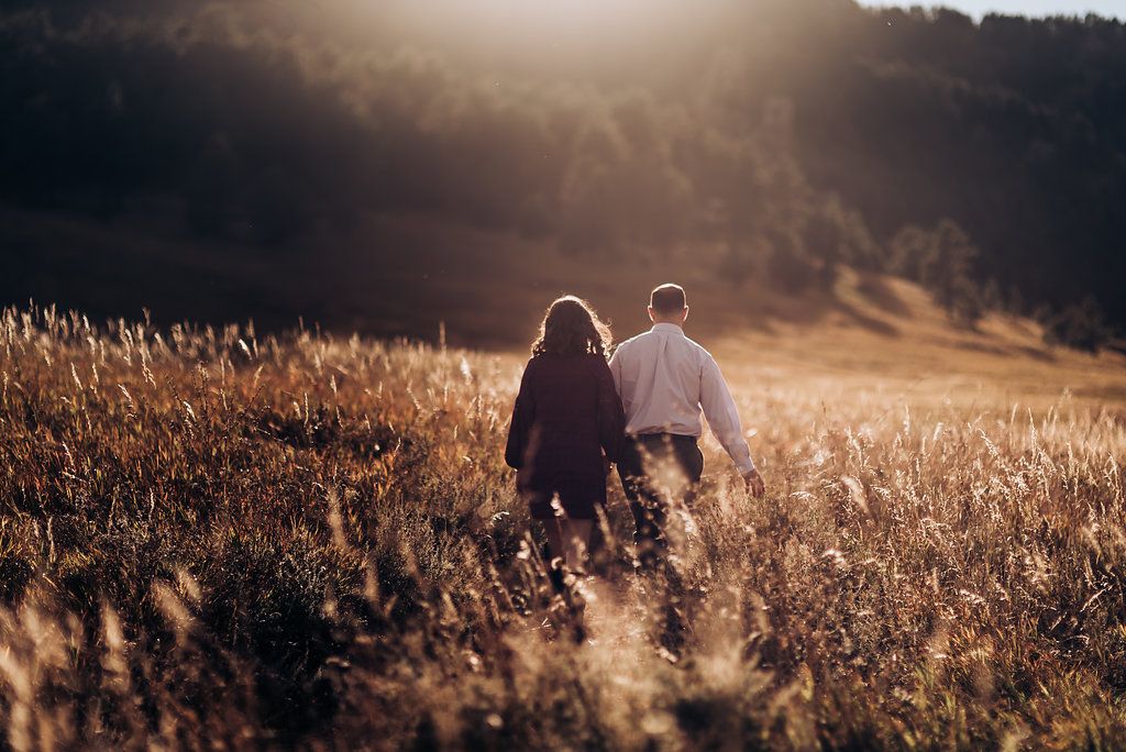 Silhouetted couple walking through golden wheat field at sunset.