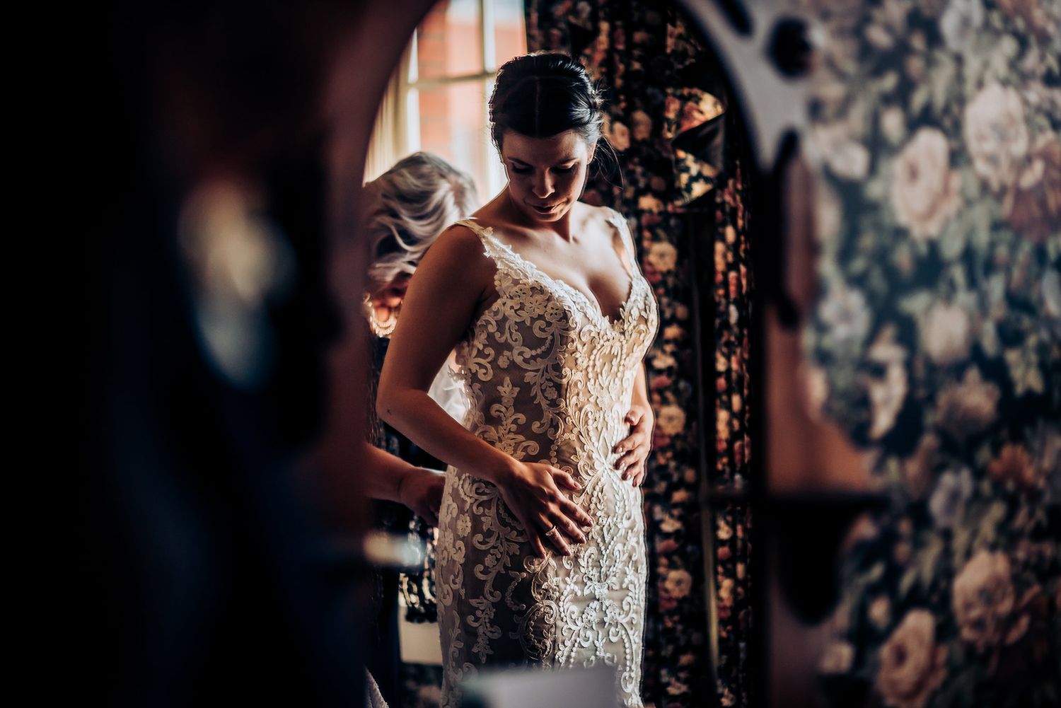 A tender moment during wedding preparations with floral wallpaper backdrop.