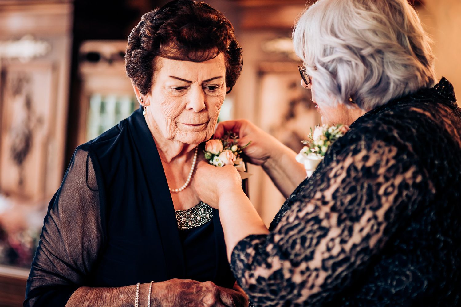 Two women in elegant black attire interact during a formal gathering.