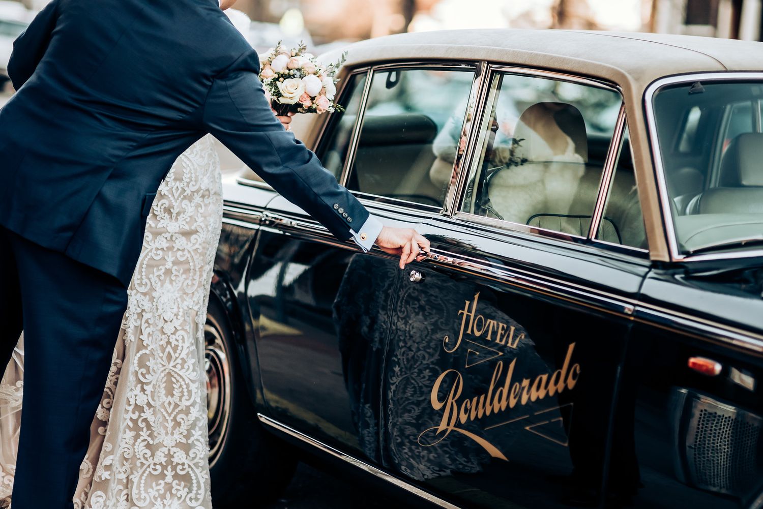 Couple entering a vintage black car with 'Just Goulderade' written on the door on their wedding day.