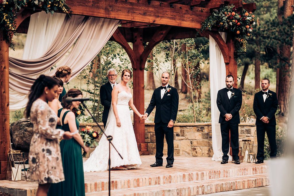 Wedding ceremony under wooden pavilion with draped fabric and stone details.