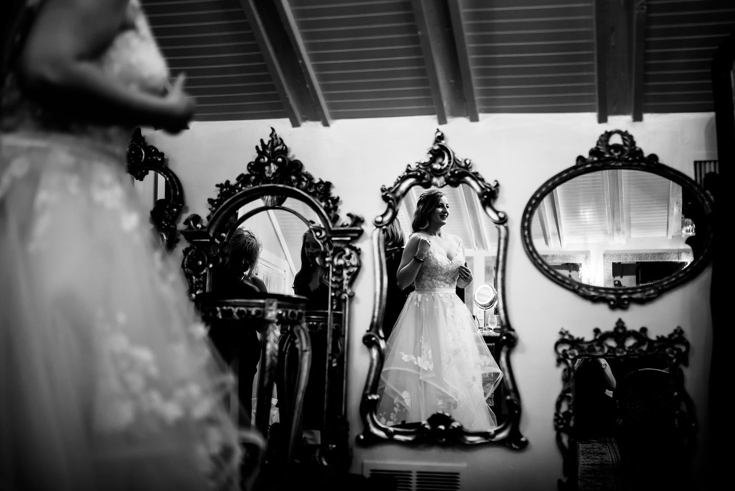 Black and white photo of ornate vintage mirrors with wedding dress reflection.