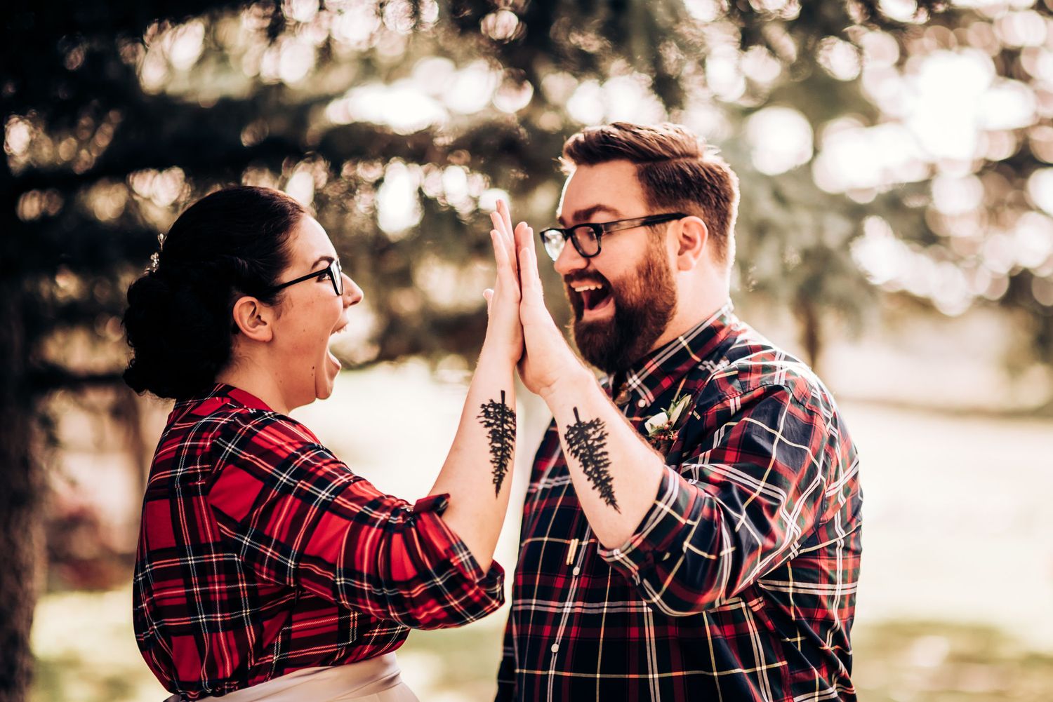 A couple in coordinating plaid outfits give each other a playful high-five outdoors.