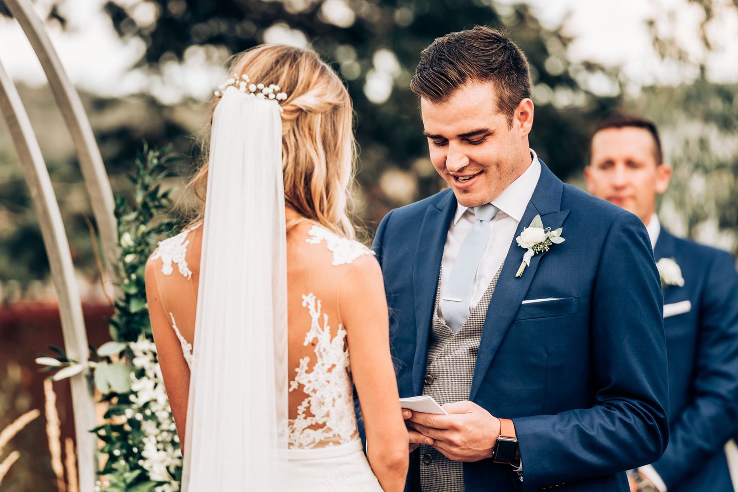 Wedding ceremony exchange of vows beneath floral arch at scenic outdoor venue.
