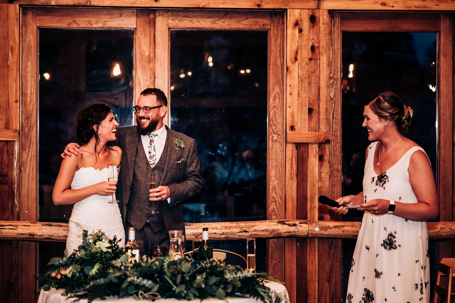 Special moment during wedding reception speeches in rustic wooden venue with large windows.