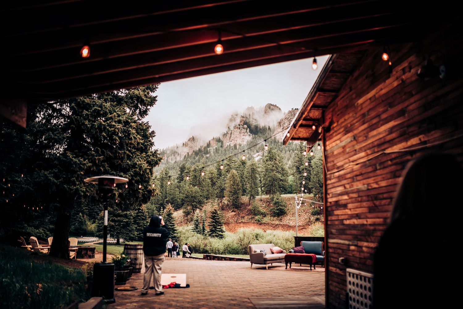 Mountain view through rustic wooden barn entrance with string lights and outdoor seating.