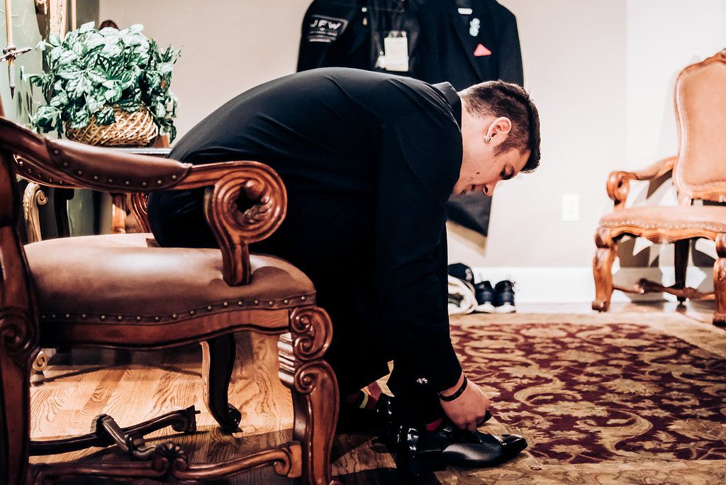Person in formal attire adjusting their shoes on an antique chair.
