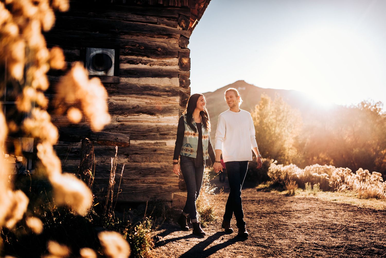 Couple standing together near rustic log cabin during sunset.