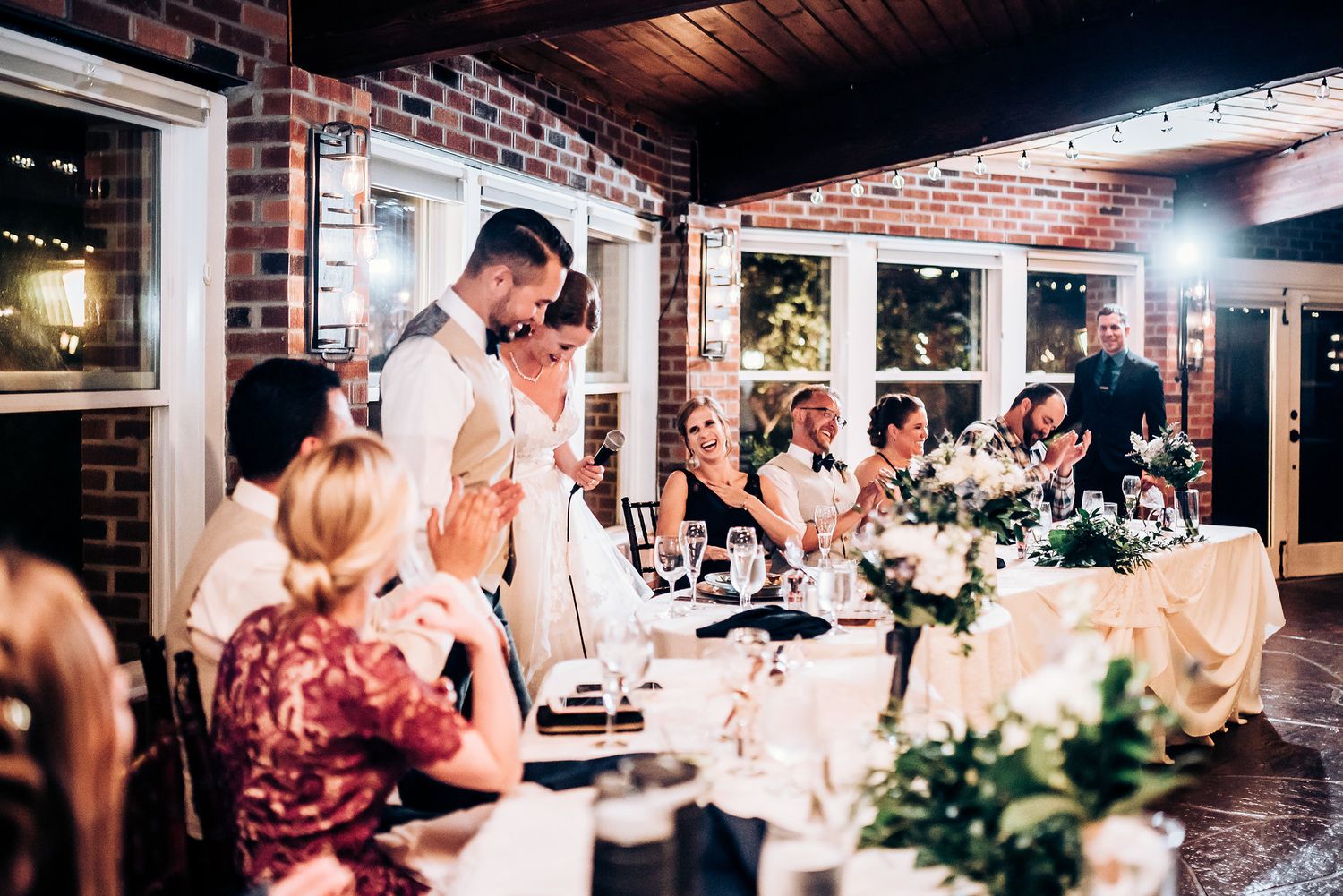 Reception celebration with guests seated at tables decorated with floral centerpieces.
