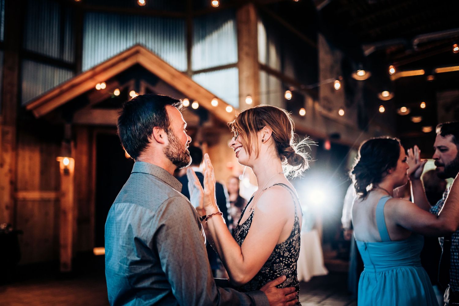 Couples slow dance intimately under twinkling lights in a rustic wooden venue.
