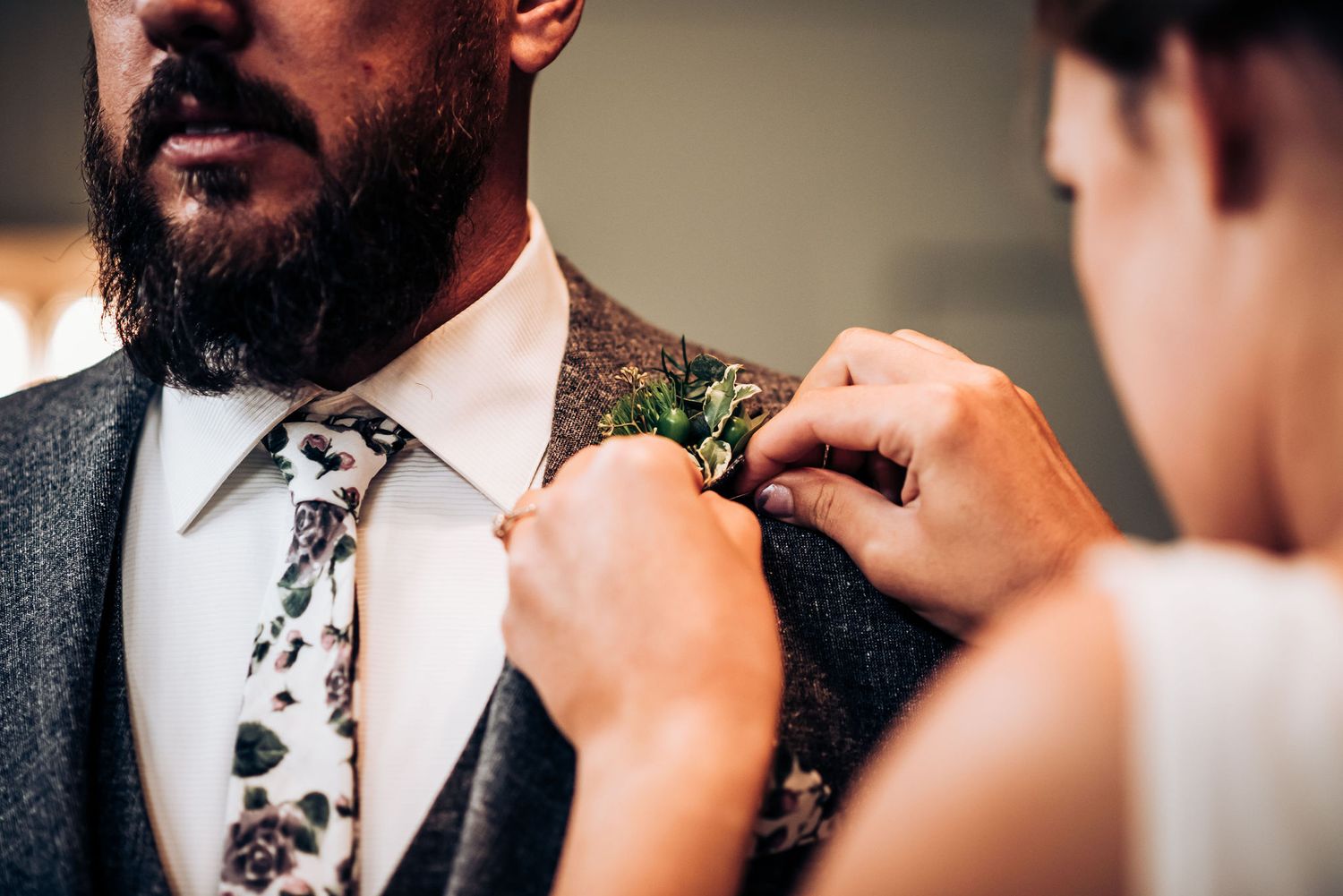 Close-up shot of hands pinning a floral boutonniere onto a grey suit lapel.