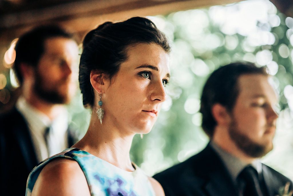 Guests stand attentively during an outdoor wedding ceremony under natural lighting.