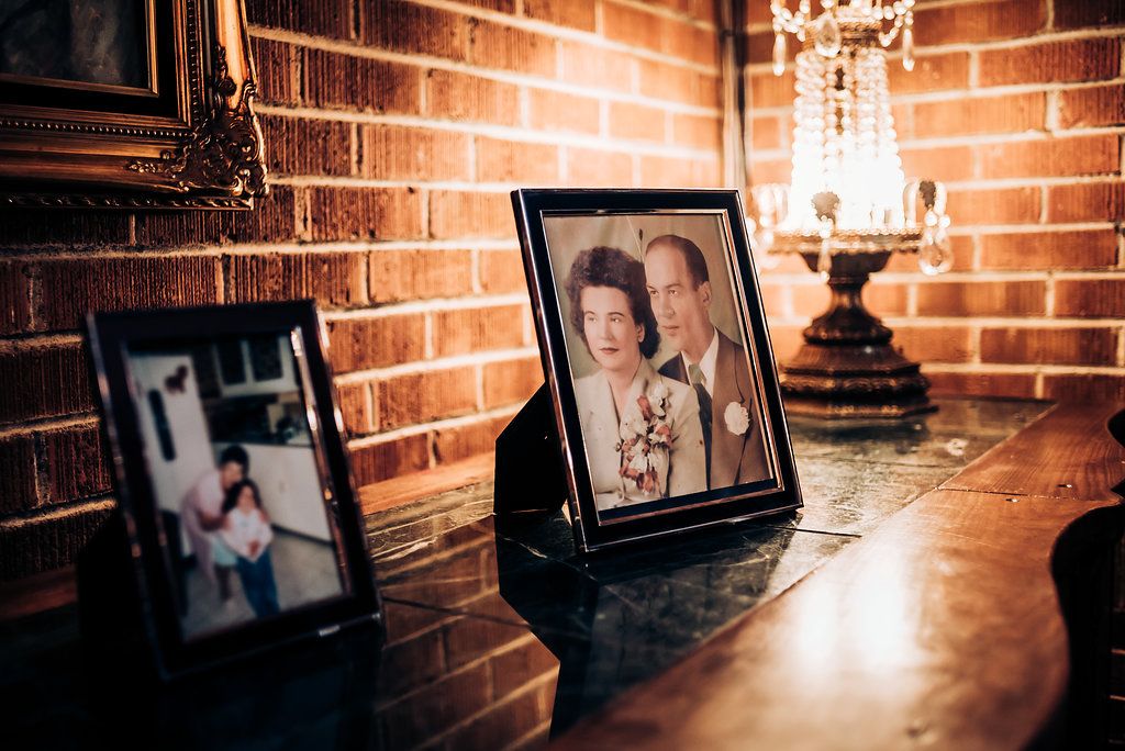 Framed photographs displayed on rustic brick ledge with antique lamp.