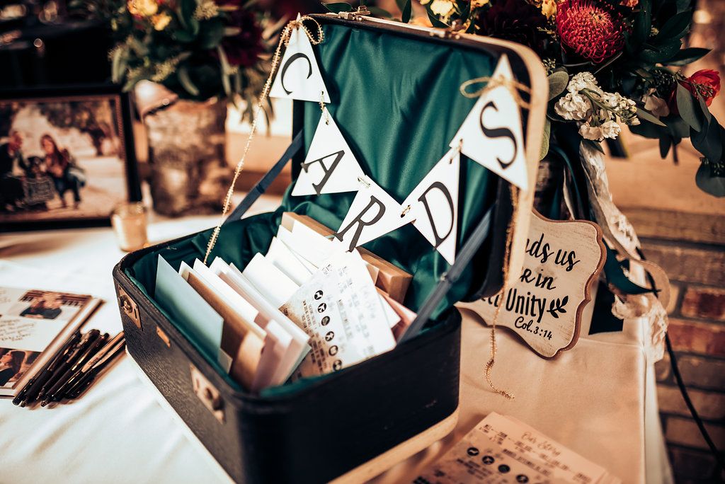 Vintage suitcase filled with wedding cards and decorative signs at reception table.