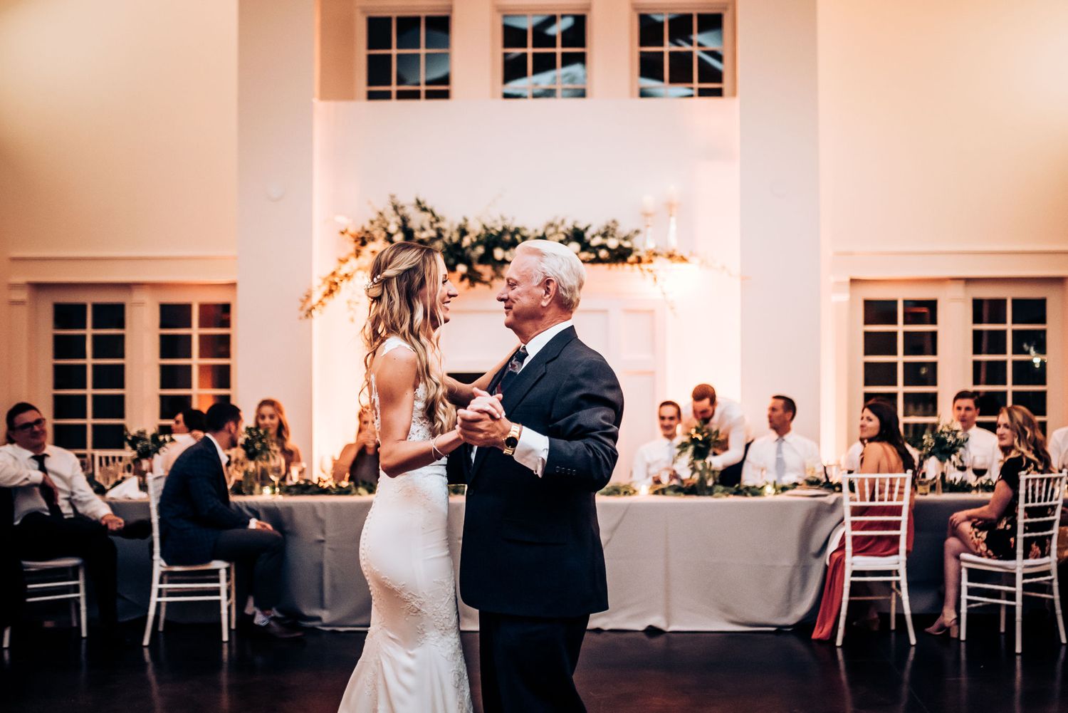 Couple dances together during their wedding reception under romantic lighting and floral decorations.