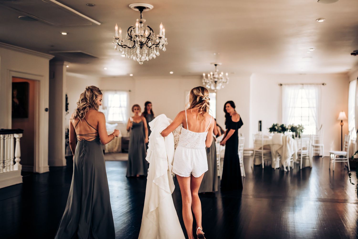 Bridesmaids helping with wedding preparations in elegant room with chandeliers.
