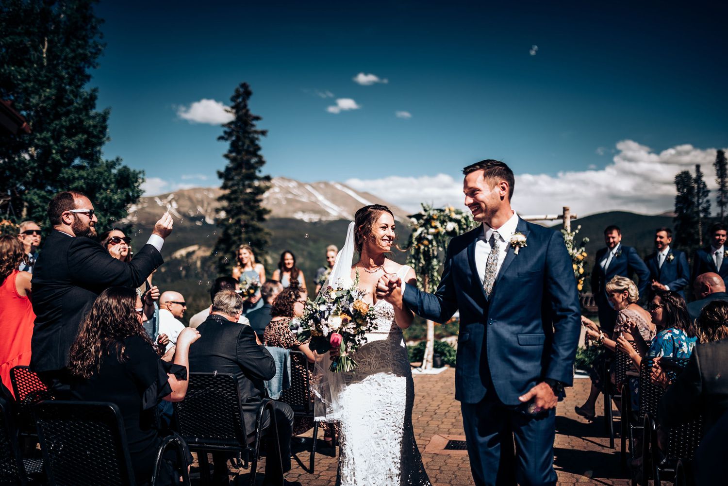 Outdoor mountain wedding ceremony with guests cheering during recessional walk.