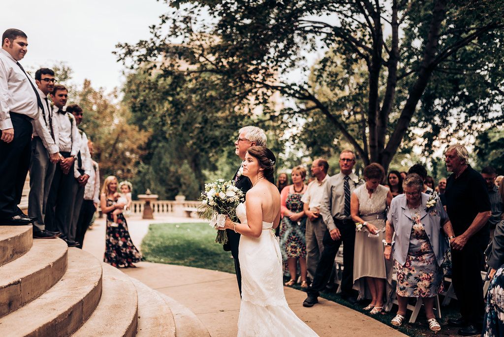 A wedding ceremony takes place on grand stone steps surrounded by trees and guests.