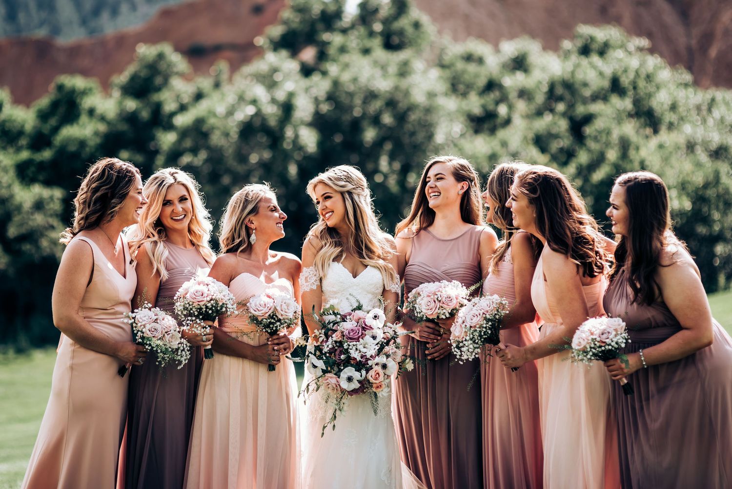 Wedding party gathered outdoors with mountain backdrop in mauve and blush colored dresses.