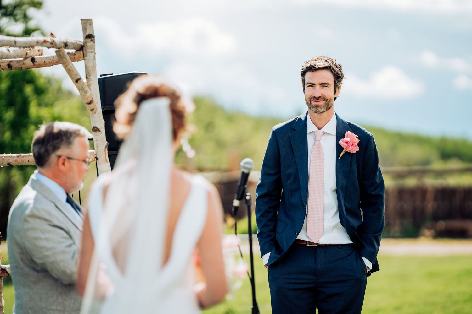 Outdoor wedding ceremony with rustic wooden arch and rolling hills in background.