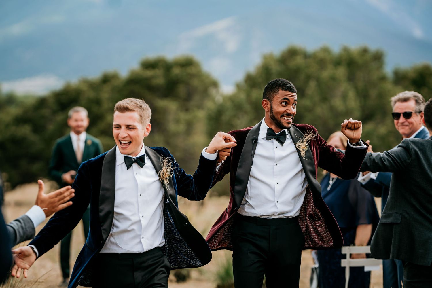 Groomsmen celebrating and cheering at an outdoor mountain wedding venue.