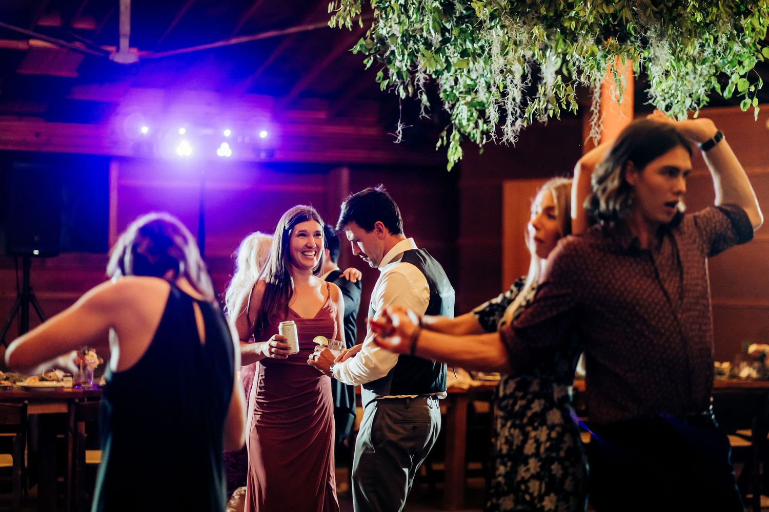 Wedding guests dancing and celebrating on the dance floor under blue lighting.