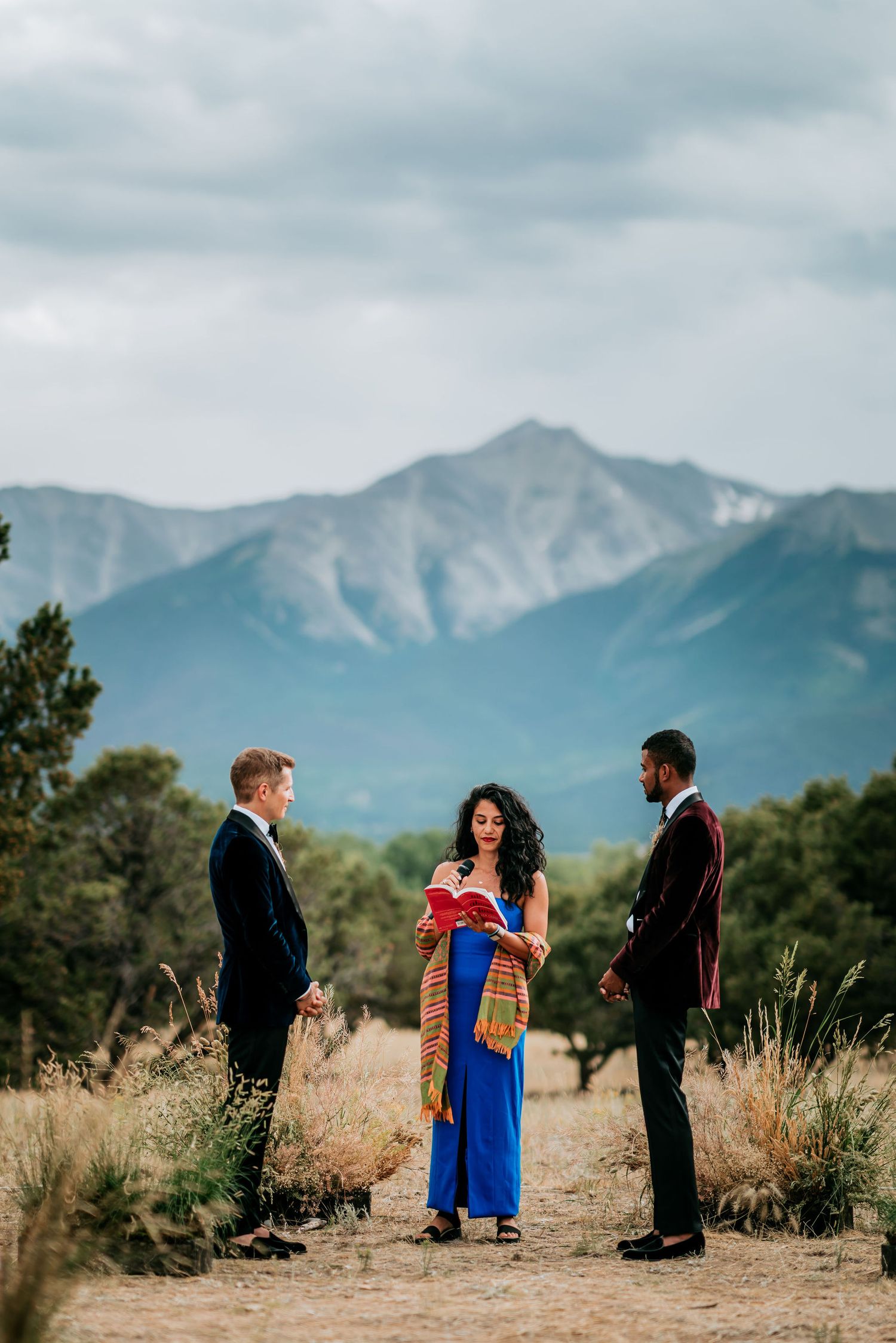 A wedding ceremony set against mountainous scenery featuring traditional dress and formal attire.
