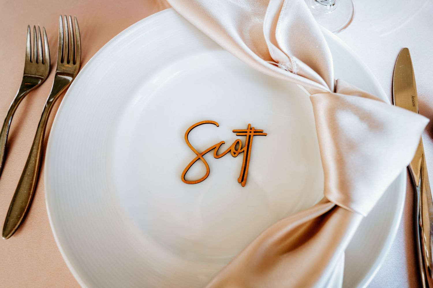 Elegant place setting with gold script and white napkin on white plate with gold utensils.