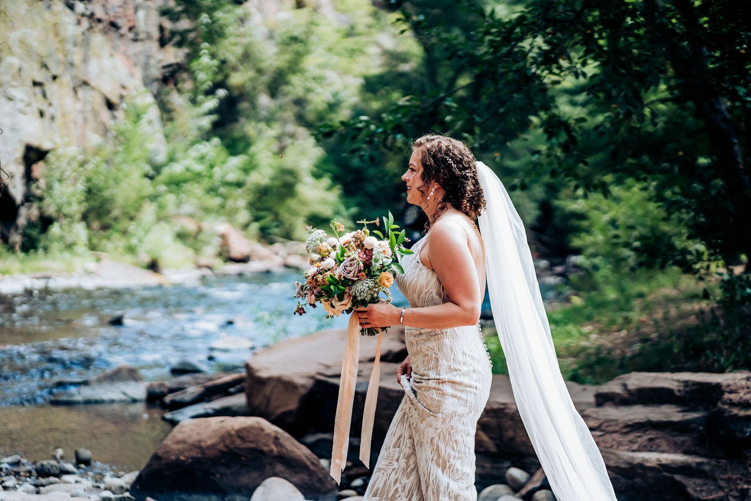 Wedding portrait by a scenic river with rocky cliffs and natural beauty.