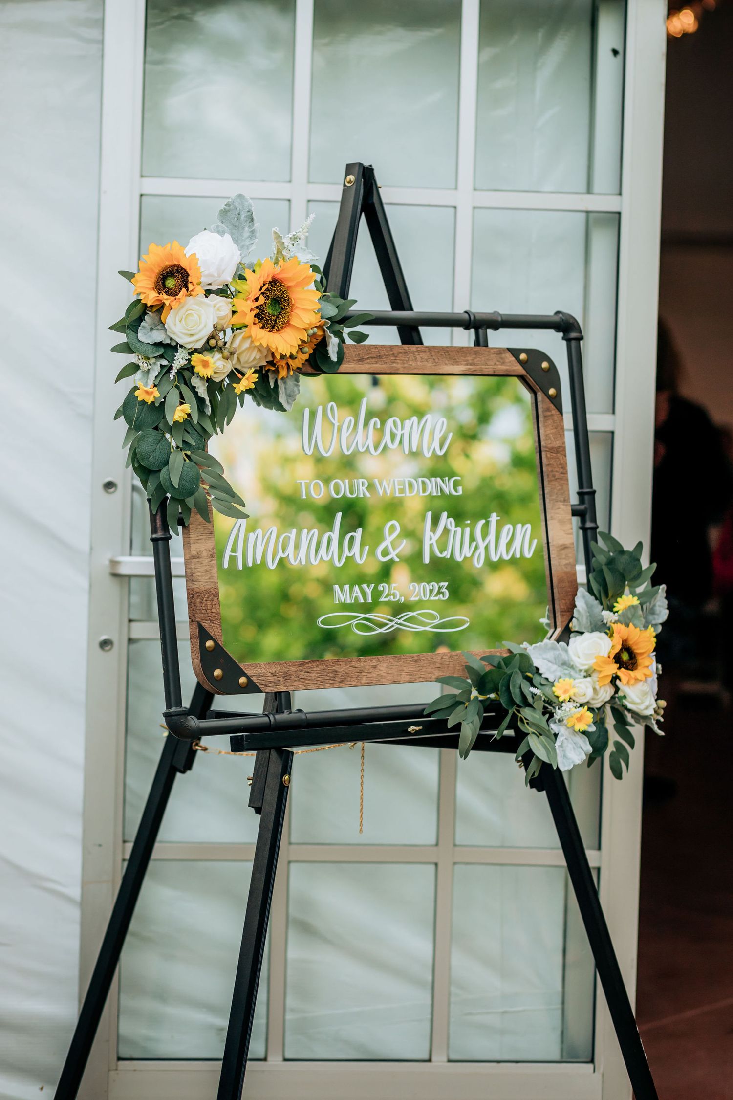Wedding welcome sign decorated with sunflowers on a black easel stand.