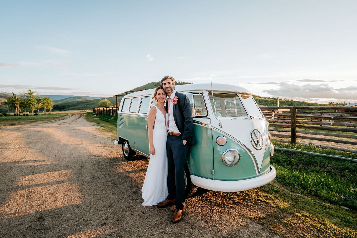 A wedding couple stands against their classic mint VW bus with mountains in the background.