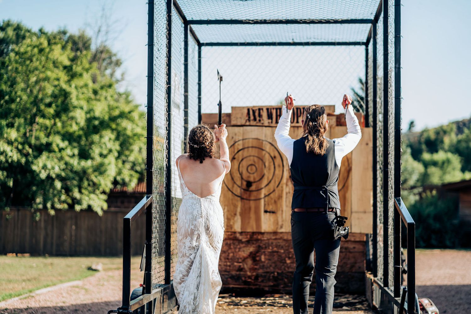 Couple practices axe throwing at wooden target during outdoor wedding activities.