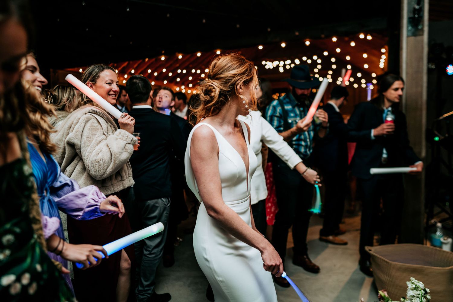 Party guests dancing and celebrating with light sticks at nighttime event.
