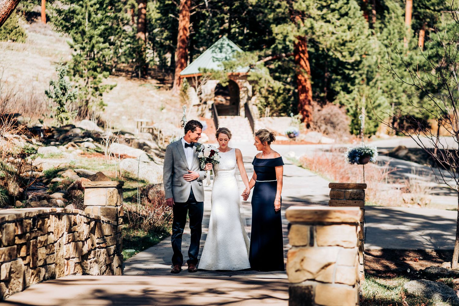 Elegant outdoor wedding scene with stone pathway and rustic gazebo in mountain forest setting.