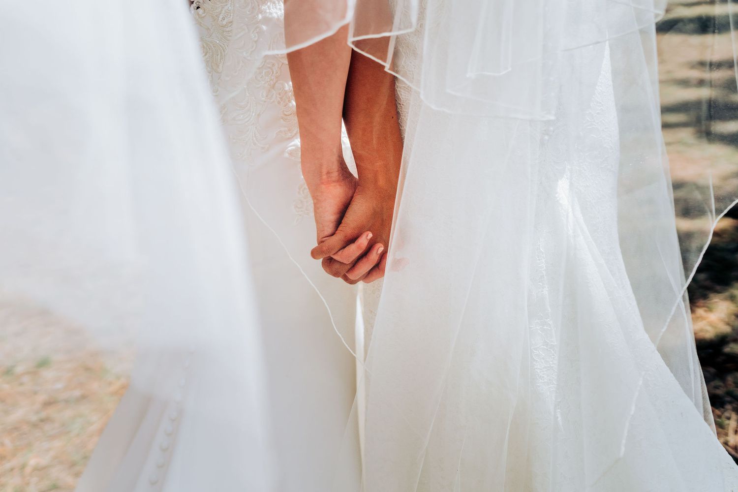 Close-up of two hands clasped together against flowing white wedding dresses.