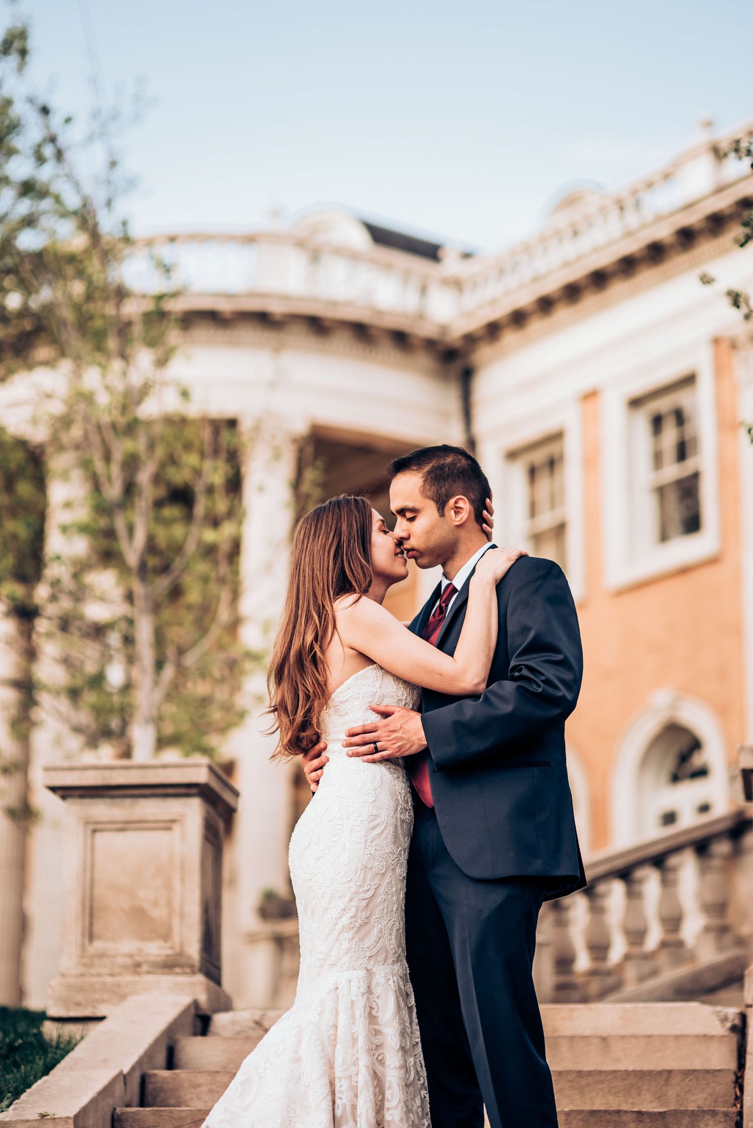 Romantic embrace on ornate stone staircase with Mediterranean architecture backdrop.