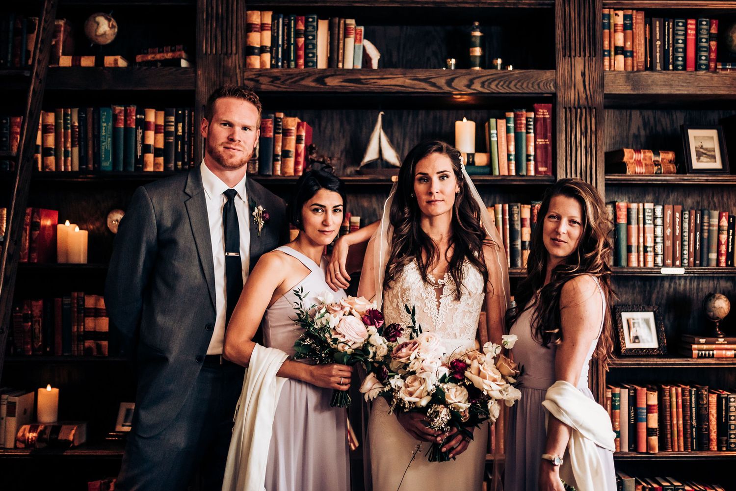 Wedding party poses in front of library shelves with elegant floral bouquets.