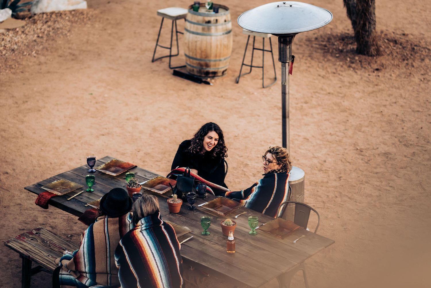 Outdoor dining setup in desert with heater lamp and rustic table settings.