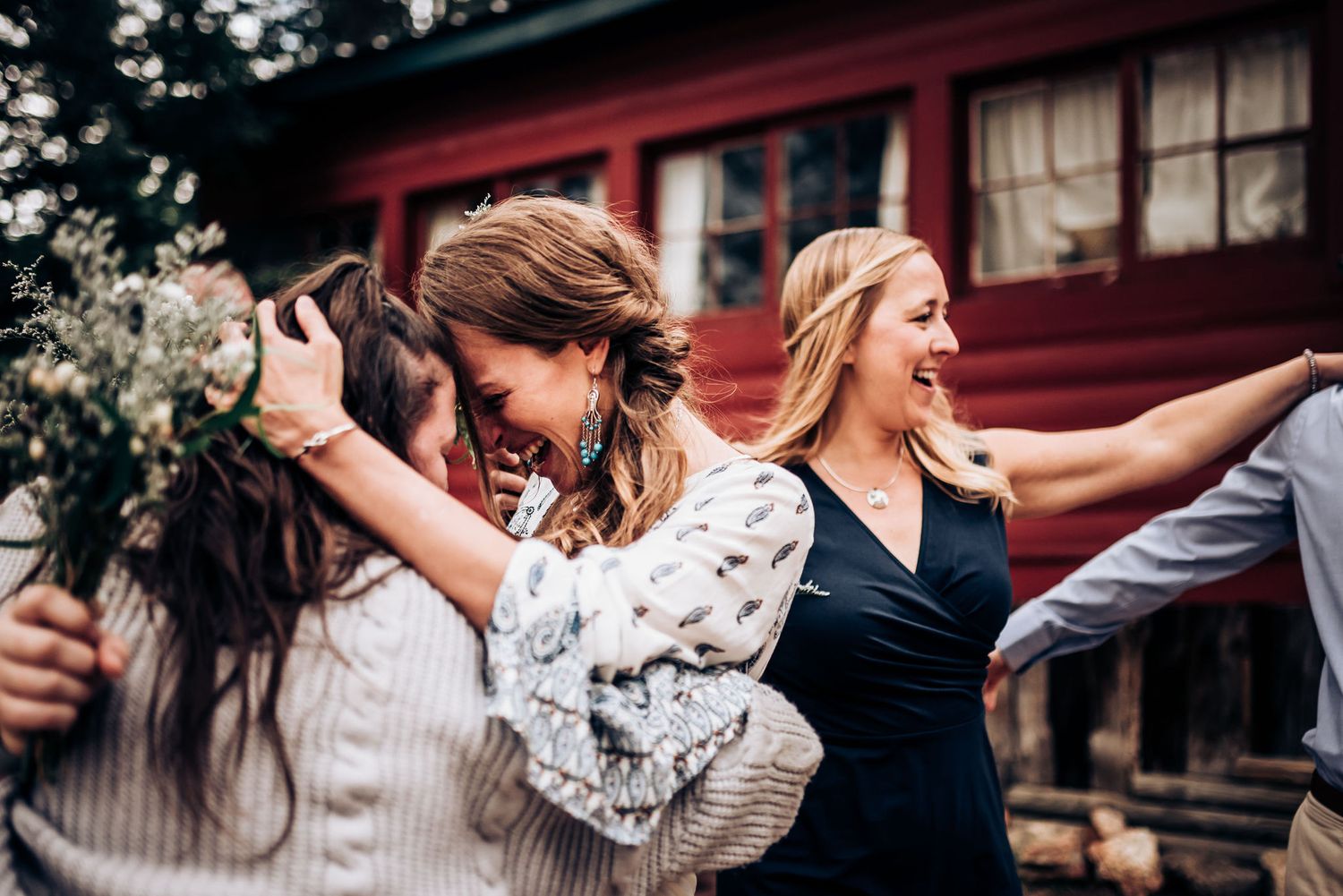 A joyful celebration with dancing and laughter outside a rustic red cabin in the woods.