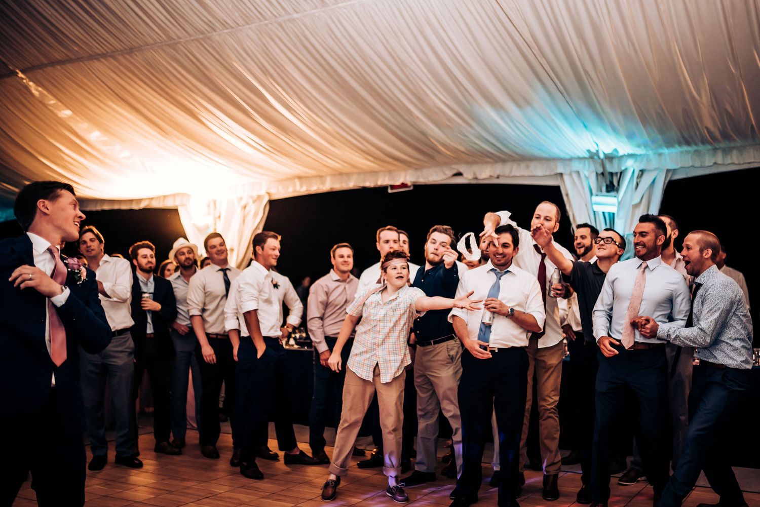 Wedding guests dancing and celebrating in formation under warm tent lighting.