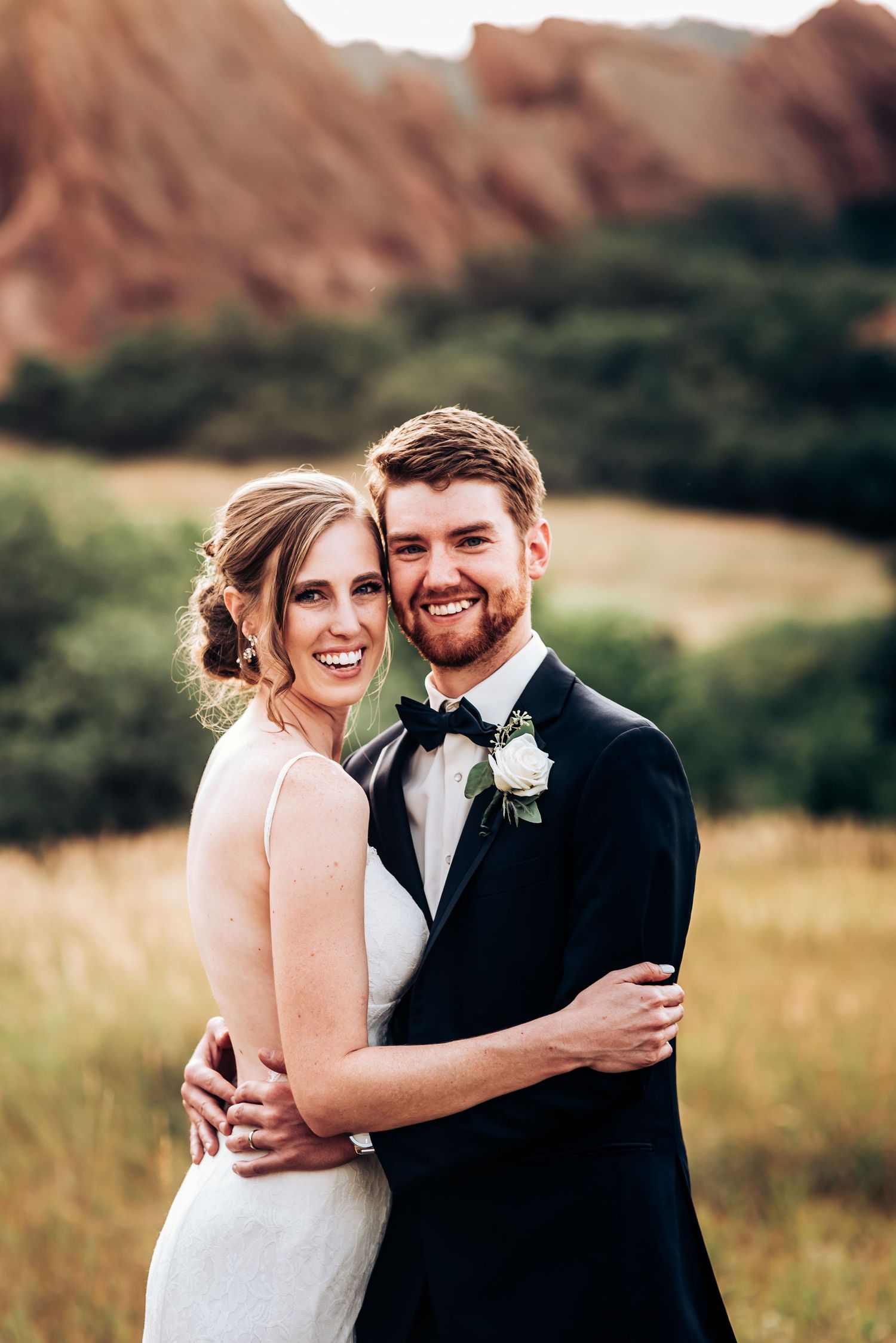 Joyful wedding portrait captured against scenic mountain landscape at golden hour.