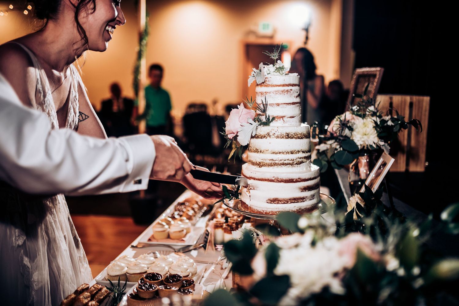 Elegant naked-style wedding cake being cut at reception.