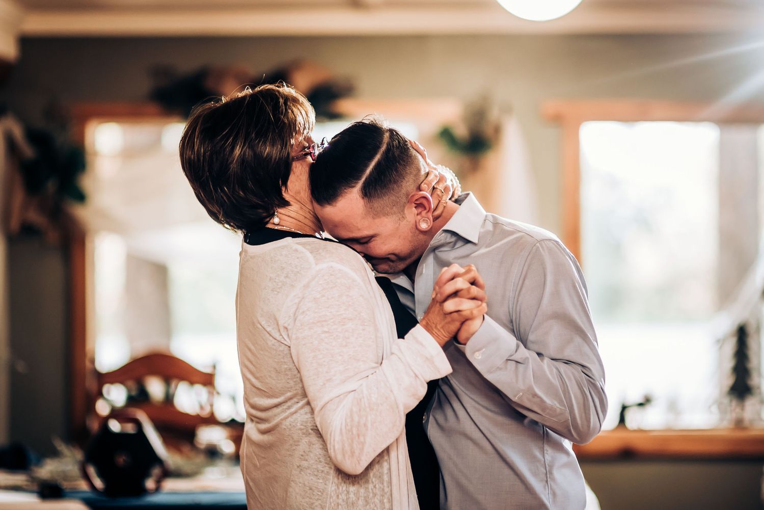Two people share an intimate slow dance together in a warmly lit indoor setting.